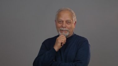 Gri stüdyo geçmişi olan düşünceli yaşlı bir adam.