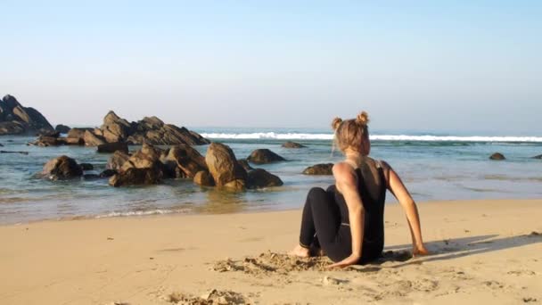 Dame oefent yoga op zandstrand tegen bruine rotsen — Stockvideo