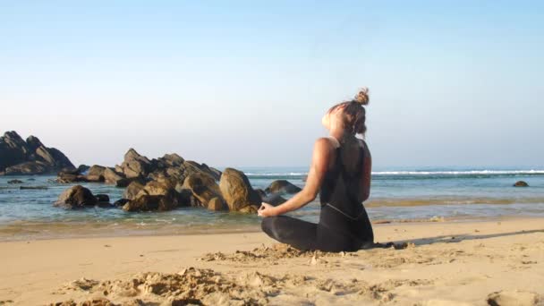 Σπορ κορίτσι τεντώνει το λαιμό σε μπλε ωκεανό με καφέ πέτρες — Αρχείο Βίντεο
