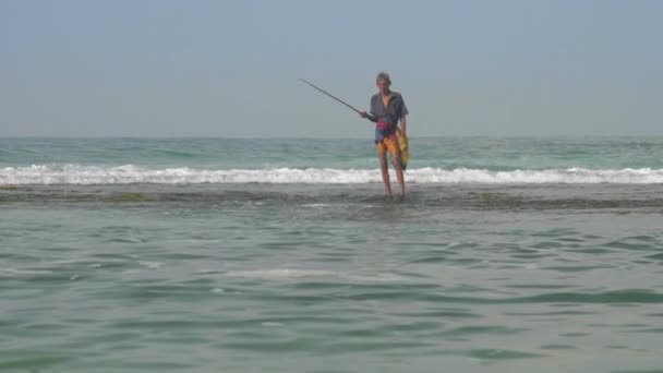 Onbeweeglijke oude man staat in het water met bruine hengel — Stockvideo