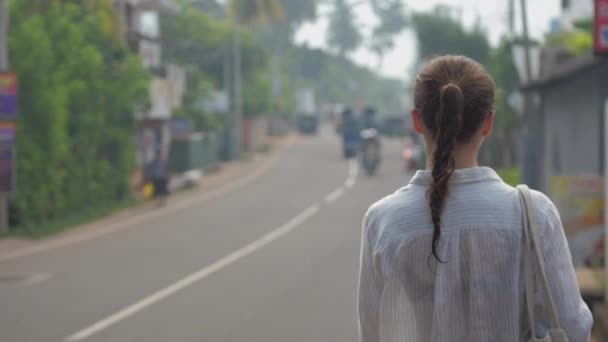 Meisje toeristische wandelingen langs straat weg tegen tropische natuur — Stockvideo