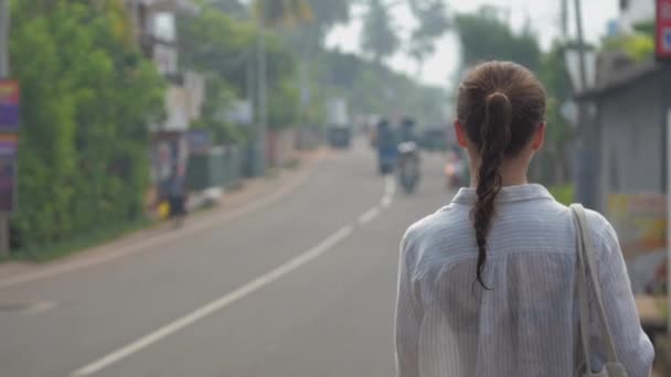 Girl tourist walks along street road against tropical nature — Stock Video