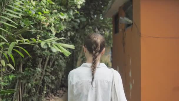 Meisje loopt langs pad tussen tropische bomen naar gebouw — Stockvideo