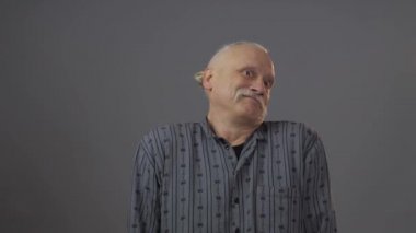 Stüdyoda şüpheli yüz ifadesi olan Avrupalı olgun bir adam koyu arka planda izole edilmiş.