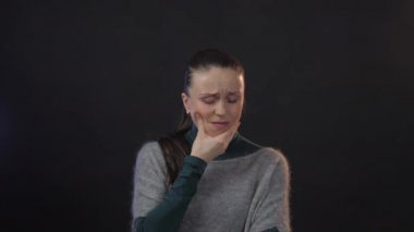 Stüdyoda diş ağrısı çeken Avrupalı yetişkin bir kadın koyu arka planda izole edilmiş.