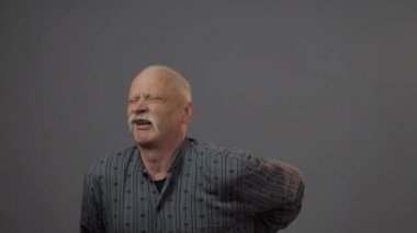 Stüdyoda sırtı ağrıyan Avrupalı olgun bir adam karanlık arka planda izole edilmiş.