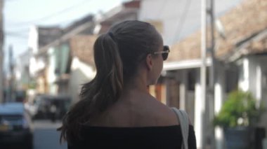 Avrupalı bir kız Sri Lanka 'da sessiz bir caddede yürüyor, ağır çekimde. Kasaba çevresindeki turizm kavramı