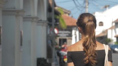 Avrupalı bir kız Sri Lanka 'da sessiz bir caddede yürüyor, ağır çekimde. Kasaba çevresindeki turizm kavramı