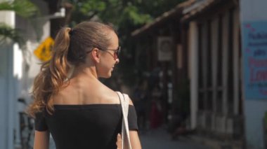 Avrupalı bir kız Sri Lanka 'da sessiz bir caddede yürüyor, ağır çekimde. Kasaba çevresindeki turizm kavramı