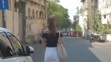 Avrupalı bir kız Sri Lanka 'da sessiz bir caddede yürüyor, ağır çekimde. Kasaba çevresindeki turizm kavramı