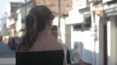 Avrupalı bir kız Sri Lanka 'da sessiz bir caddede yürüyor, ağır çekimde. Kasaba çevresindeki turizm kavramı