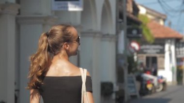 Avrupalı bir kız Sri Lanka 'da sessiz bir caddede yürüyor, ağır çekimde. Kasaba çevresindeki turizm kavramı