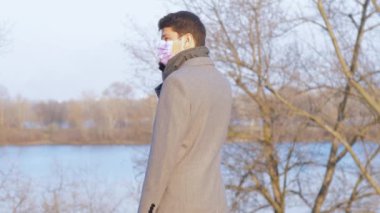 Tıp maskeli Avrupalı adam şehir parkında akıllı telefondan konuşuyor.