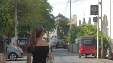 Avrupalı bir kız Sri Lanka 'da sessiz bir caddede yürüyor, ağır çekimde. Kasaba çevresindeki turizm kavramı
