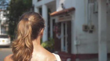 Avrupalı bir kız Sri Lanka 'da sessiz bir caddede yürüyor, ağır çekimde. Kasaba çevresindeki turizm kavramı