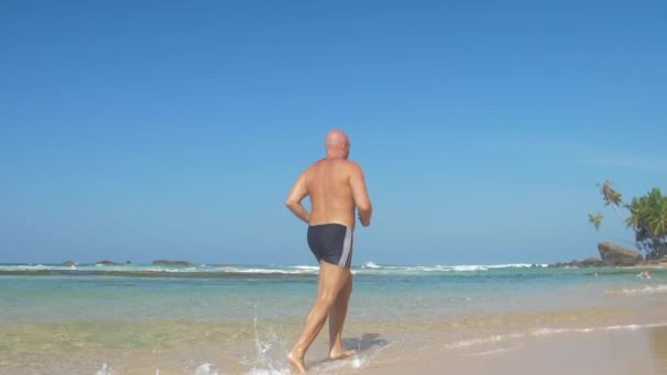 欧洲成年男子在靠近海洋的沙滩上慢跑 白天阳光灿烂 海浪汹涌 — 图库视频影像