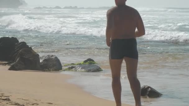 欧洲成年男子在靠近海洋的沙滩上慢跑 白天阳光灿烂 海浪汹涌 — 图库视频影像