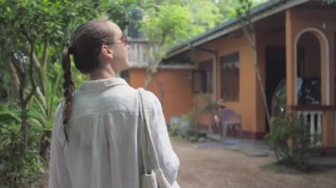 Kız, tropikal ağaçların arasında binaya doğru yürüyor.