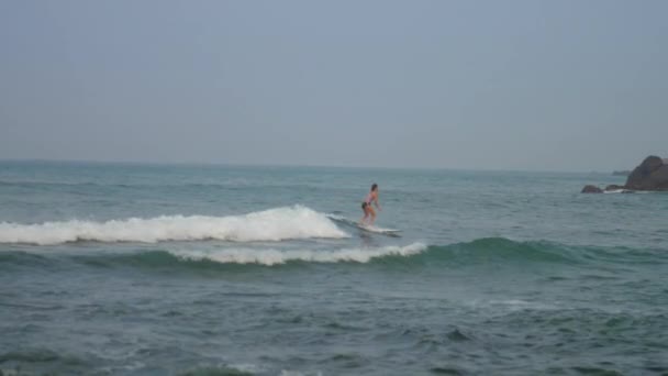 Vrouw vangt golf staande op surfplank tegen landschap — Stockvideo