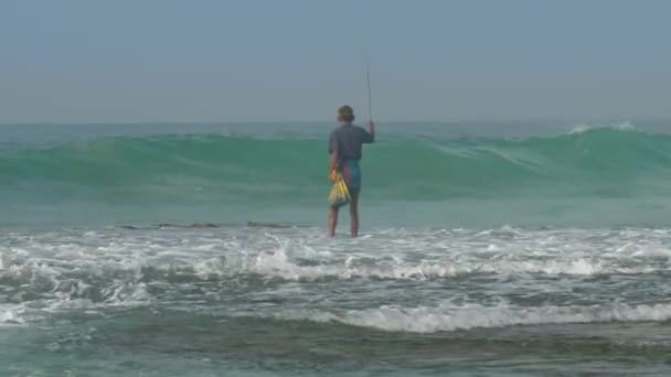 Pescador camina a lo largo de borde de surf de agua en olas marinas espumosas — Vídeo de stock