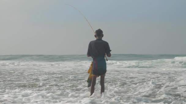 Pescatore sta in acqua schiumosa oceano sotto cielo nuvoloso — Video Stock