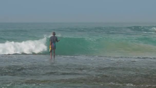 Fisherman walks along water surf edge at foaming ocean waves — Stock Video