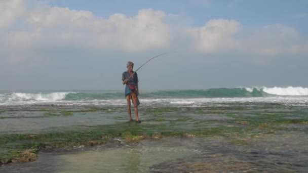 Rybář stojí v zpěněném oceánu na zelených řasách pomalu — Stock video