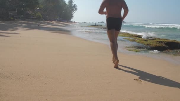 Homem mantém em forma jogging ao longo da praia contra ondas do oceano — Vídeo de Stock