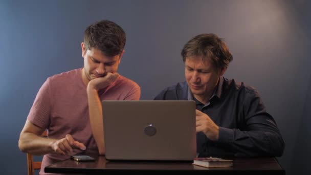 Мужчина с телефоном рядом со старшим отцом учится пользоваться ноутбуком — стоковое видео