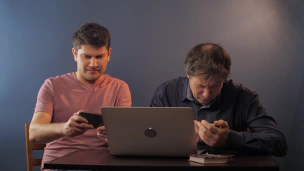 Мужчина наслаждается игрой на смартфоне, пока отец учится пользоваться телефоном — стоковое видео