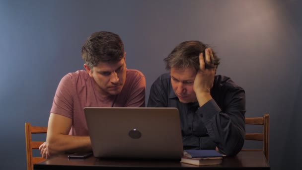 Συμπυκνωμένος γιος με τον πατέρα εργάζονται μαζί σε σύγχρονο φορητό υπολογιστή — Αρχείο Βίντεο