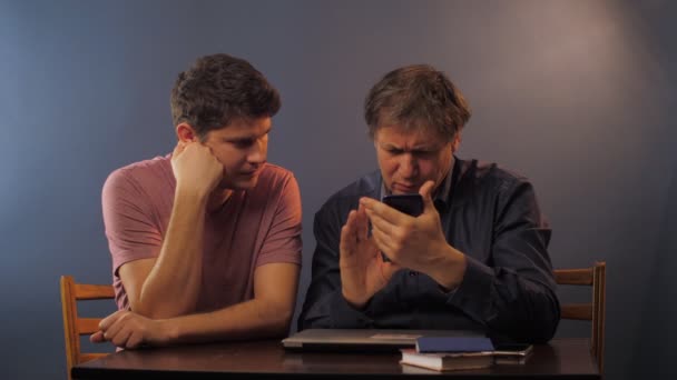 Man helps father to surf internet with smartphone at table — Stock Video