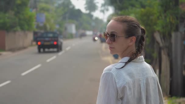 Молодая женщина стоит на дороге, оглядываясь на проезжающий городской автобус — стоковое видео
