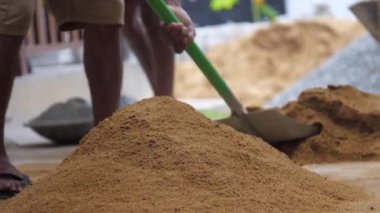 Biri sarı kumu kapar ve kürekle yığına atar.