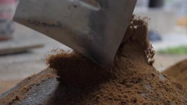 İşçi metal kürekle karıştırmadan önce çimentoya kum ekler.