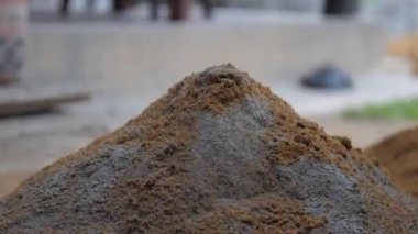 İşçi metal kürekle karıştırmadan önce çimentoya kum ekler.