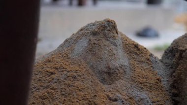 İşçi metal kürekle karıştırmadan önce çimentoya kum ekler.