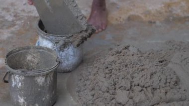 İşçi, metal kürekle eski kovalara ıslak çimento koyar.