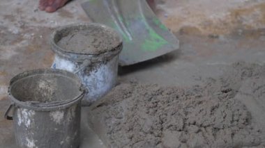 İşçi, metal kürekle eski kovalara ıslak çimento koyar.