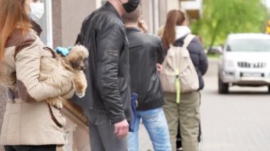 Tek kullanımlık maskeli esmer ve eldivenli kadın, köpeği kuyrukta tutuyor.