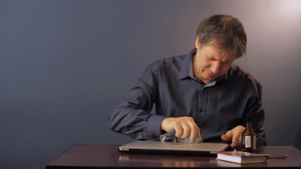 Volwassen man in shirt doekjes laptop met alcohol aan kleine tafel — Stockvideo