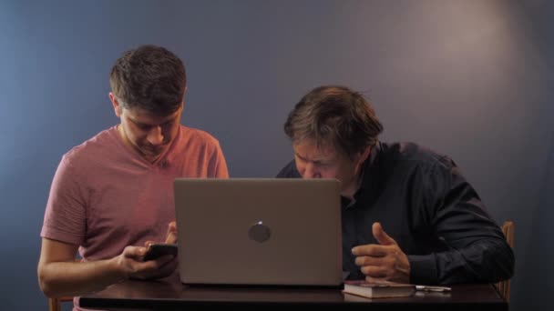 Хлопець використовує телефон старший чоловік вивчає ноутбук за столом в кімнаті — стокове відео