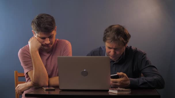 Babası olan adam masadaki bilgisayarın yanında akıllı telefon kullanıyor. — Stok video