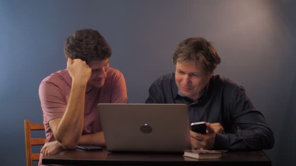 Fils souriant enseigne père aîné à travailler sur ordinateur portable à la table — Video