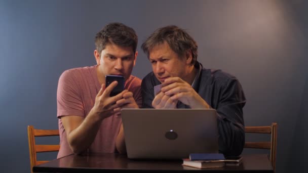 Sohn mit Vater gibt Informationen auf Smartphone am Tisch ein — Stockvideo