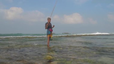 Balıkçı, yeşil yosunların köpüklü okyanusunda duruyor.