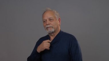 Kafası karışmış yaşlı adam düz görünüyor ve mavi süveteri tamir ediyor.