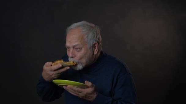 Excited old man in blue pullover eats pizza holding plate — Stock Video