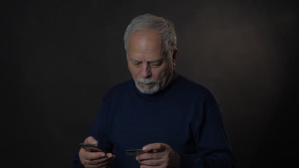 Serious old man in blue pullover types credit card data — Stock Video