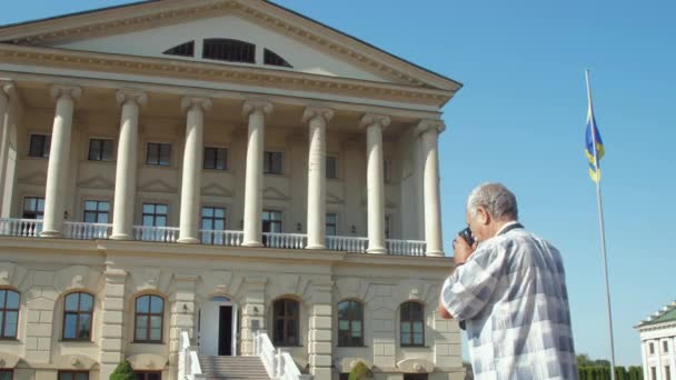 Старший чоловік тримає камеру і фотографує величний палац — стокове відео